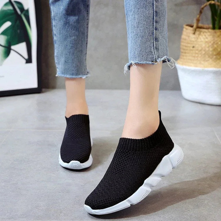 Black knit slip-on sneakers with white sole worn with cropped frayed hem jeans