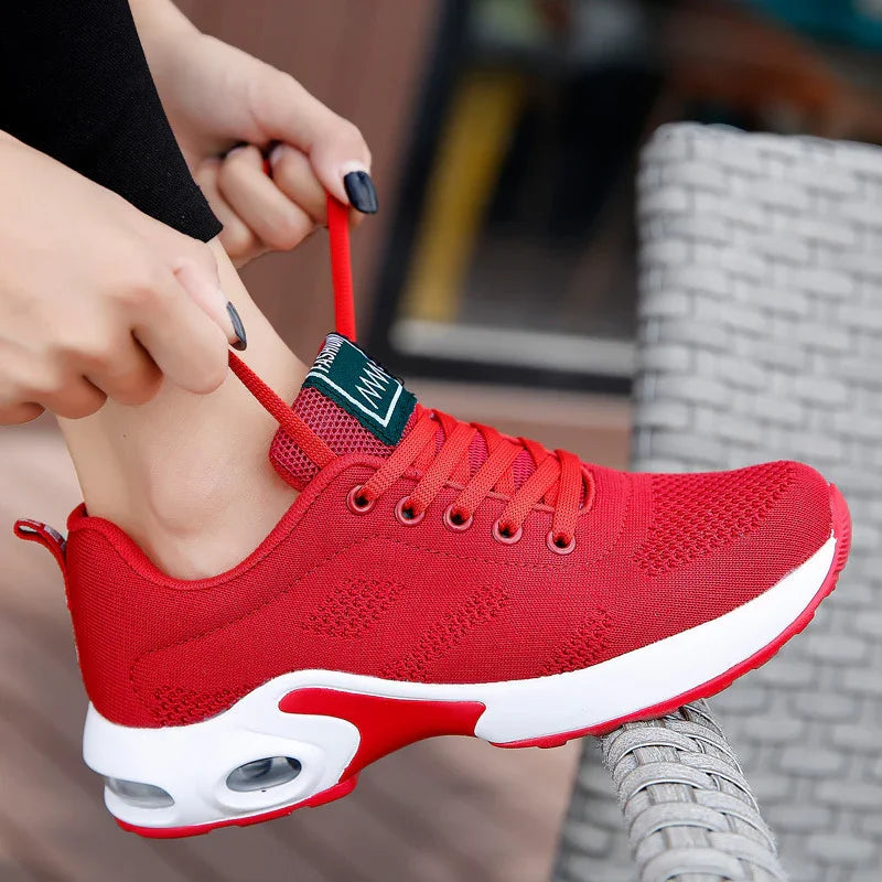 Person tying bright red breathable mesh athletic sneaker with white sole outdoors