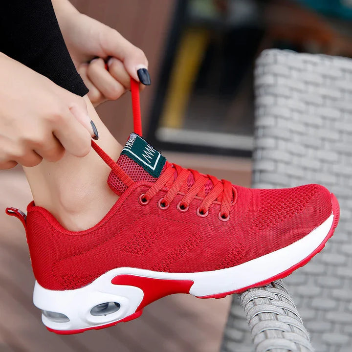 Person tying bright red breathable mesh athletic sneaker with white sole outdoors
