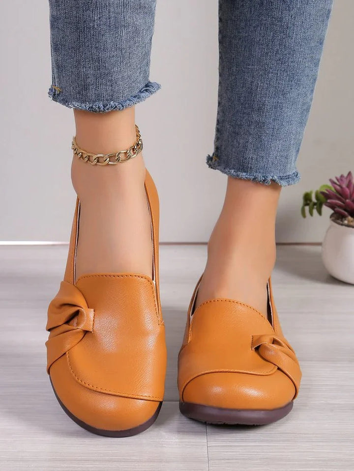 Close-up of feet wearing tan leather slip-on flats with bow detail and cropped frayed hem jeans