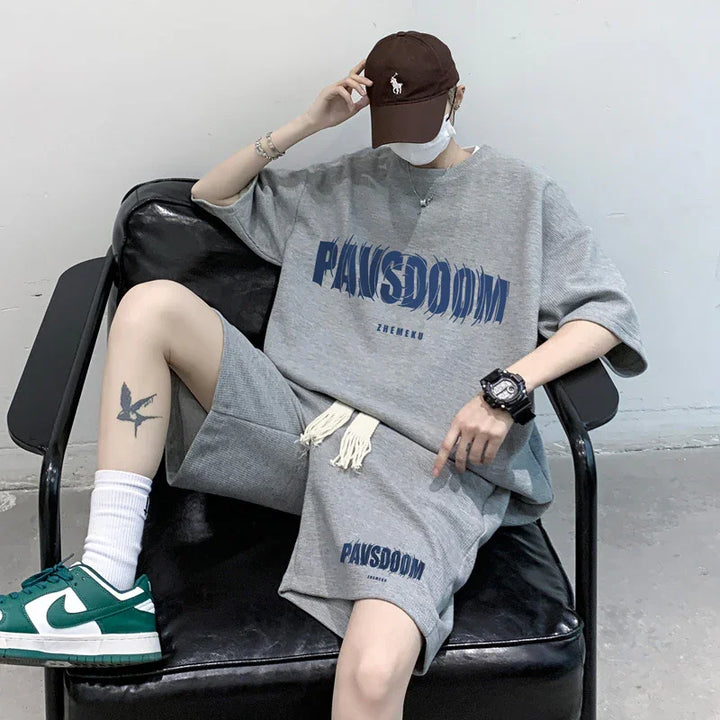 Person wearing grey oversized PAWSDOOM t-shirt and shorts, green white sneakers, sitting on black chair