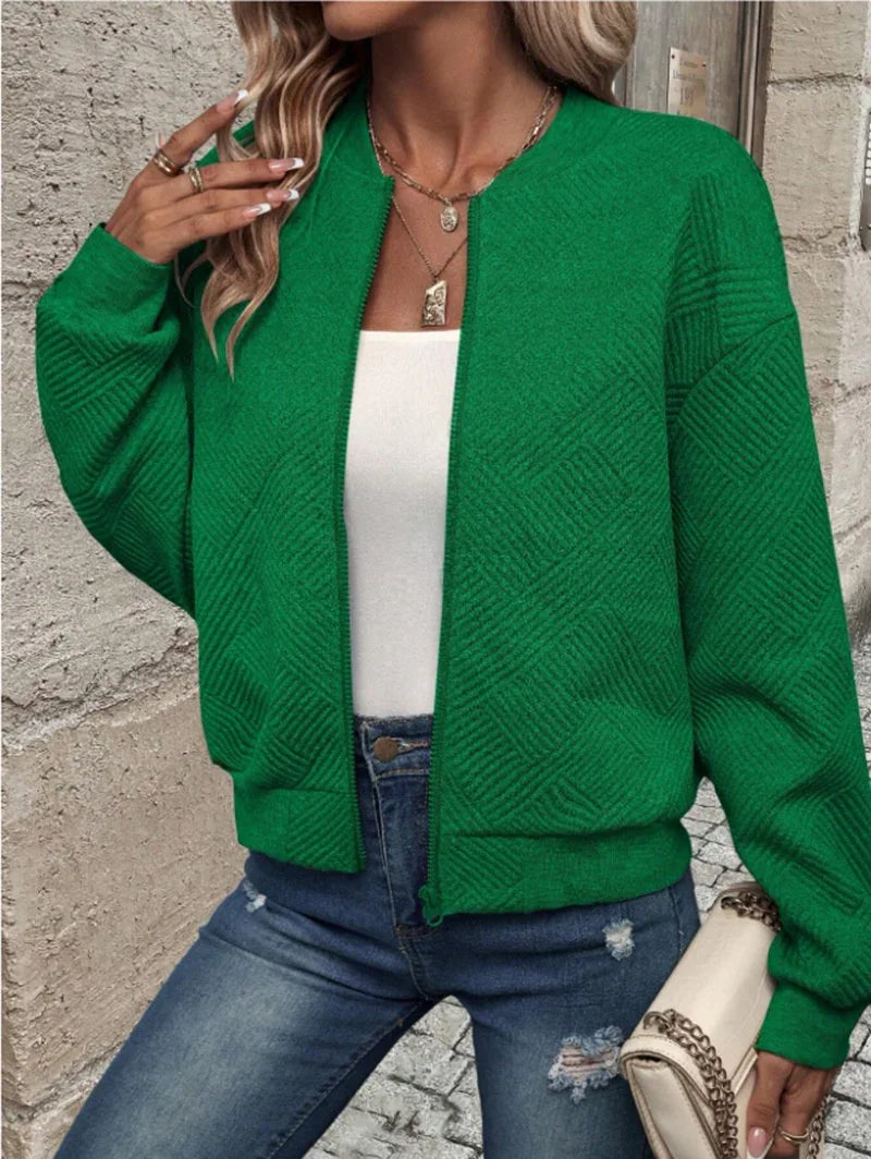 Woman wearing green textured knit cardigan with white top and ripped blue jeans holding beige chain handbag