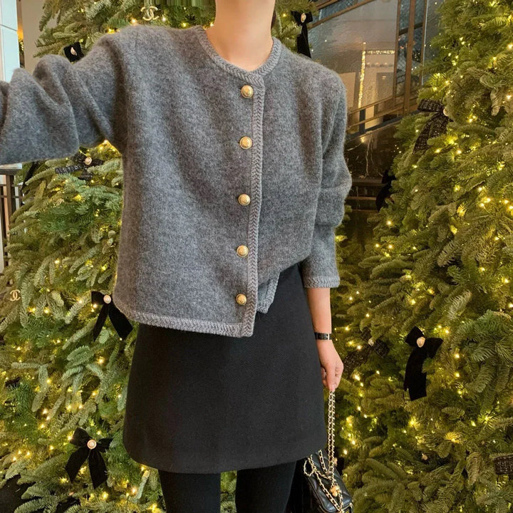Woman in grey buttoned cardigan and black skirt standing by decorated Christmas trees with lights and black bows