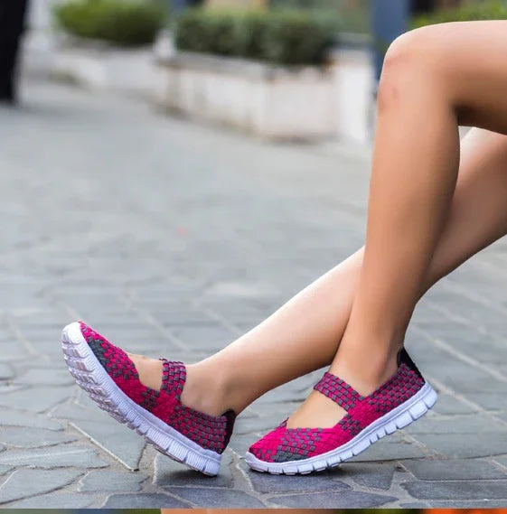 Woman wearing pink and black woven casual shoes with white soles sitting on pavement outdoors