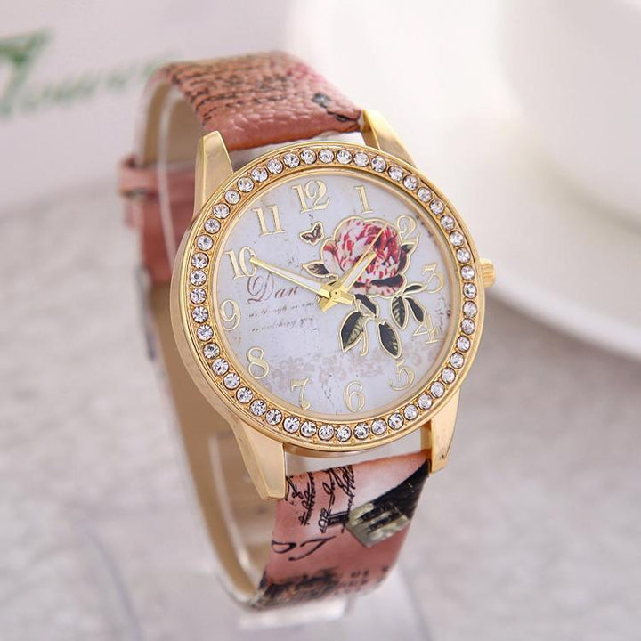 Elegant gold-tone wristwatch with rhinestone bezel, floral dial design, and pink patterned strap