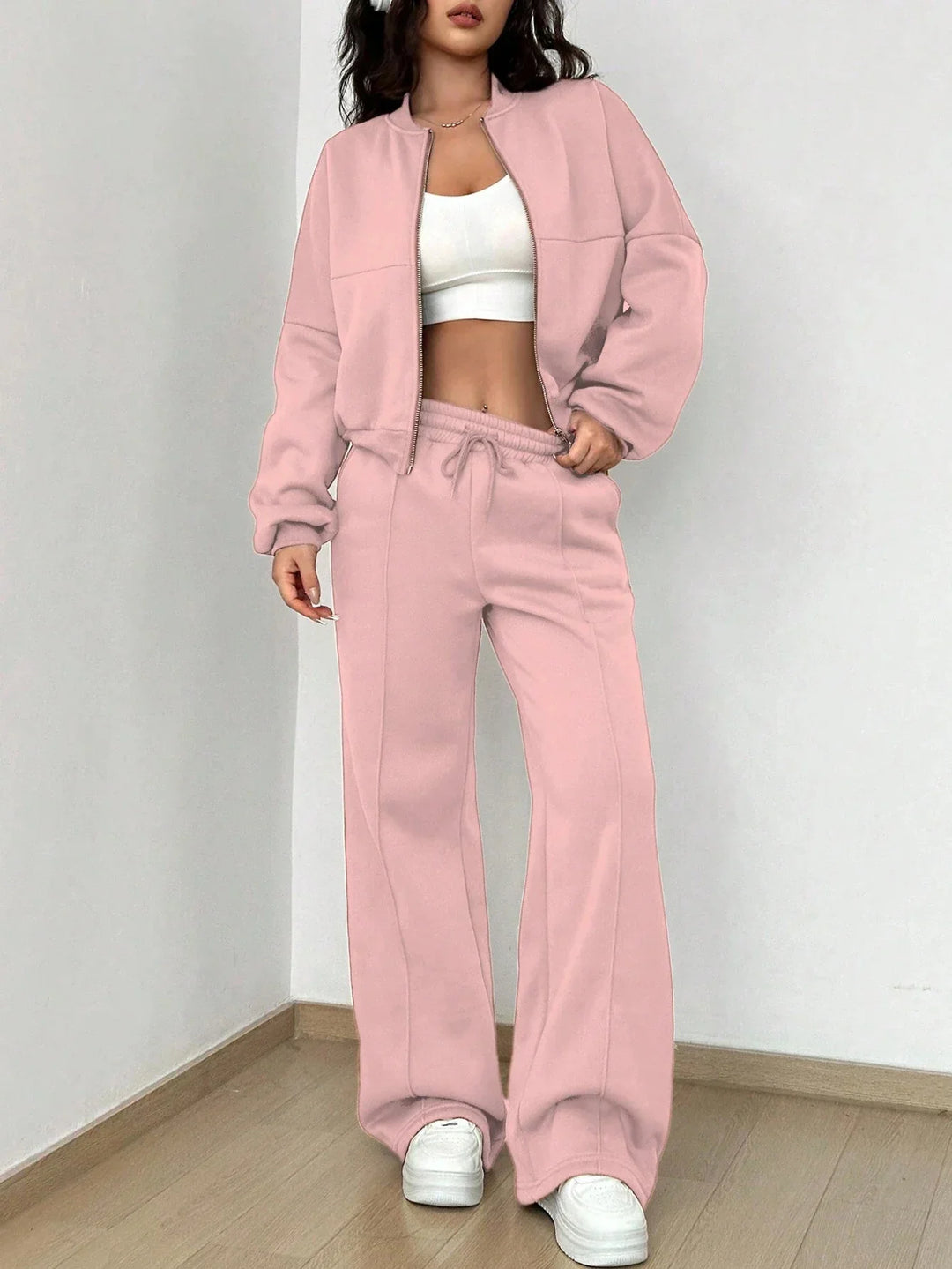 Woman wearing a pink tracksuit with a zip-up jacket and wide-leg pants, paired with a white crop top and sneakers