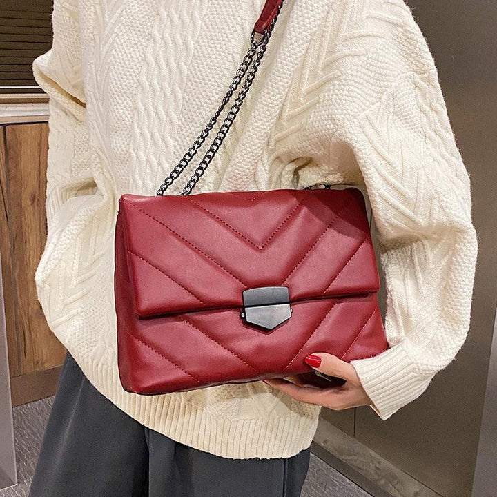 Red quilted leather shoulder bag with black clasp and chain strap, held by person in white knit sweater