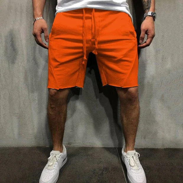 Man wearing bright orange casual shorts with drawstring and white sneakers against gray wall