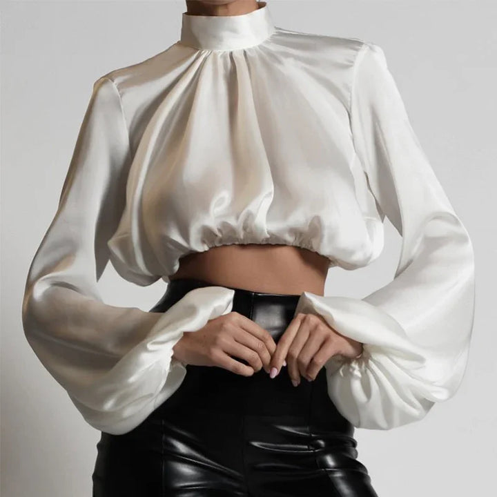 White satin cropped blouse with high neck and puffed long sleeves paired with black leather pants