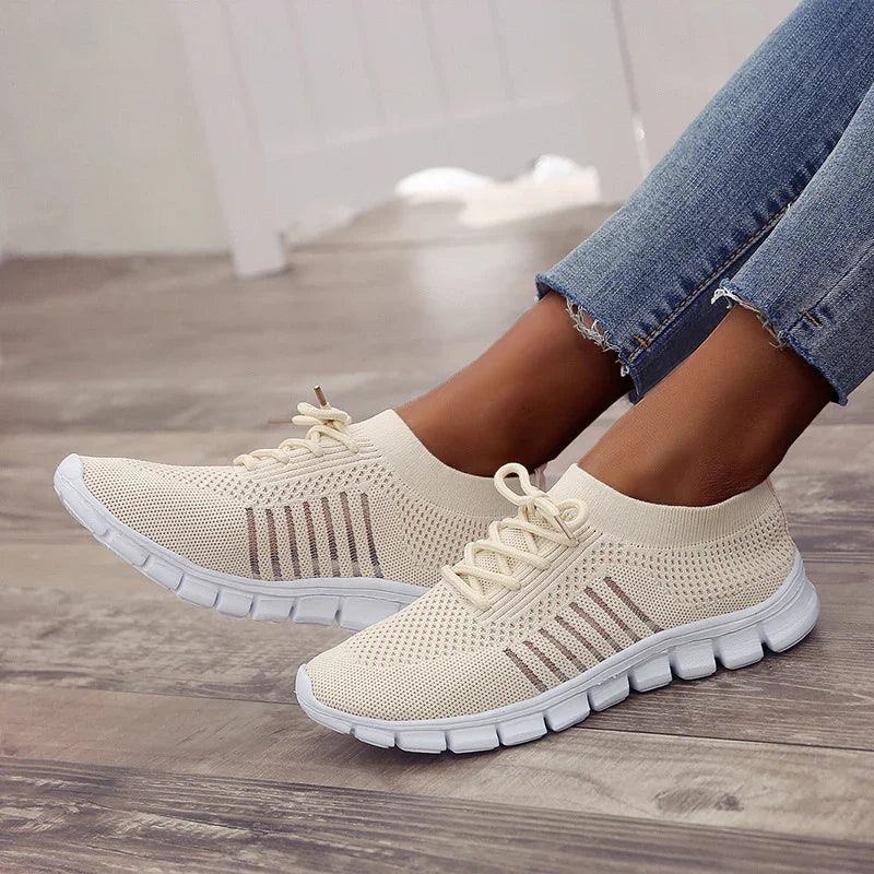 Light beige knit slip-on sneakers with white flexible sole worn with frayed hem blue jeans on wooden floor