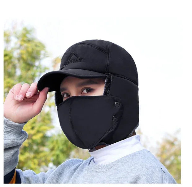Person wearing black trapper hat with attached face mask and ear flaps in outdoor setting
