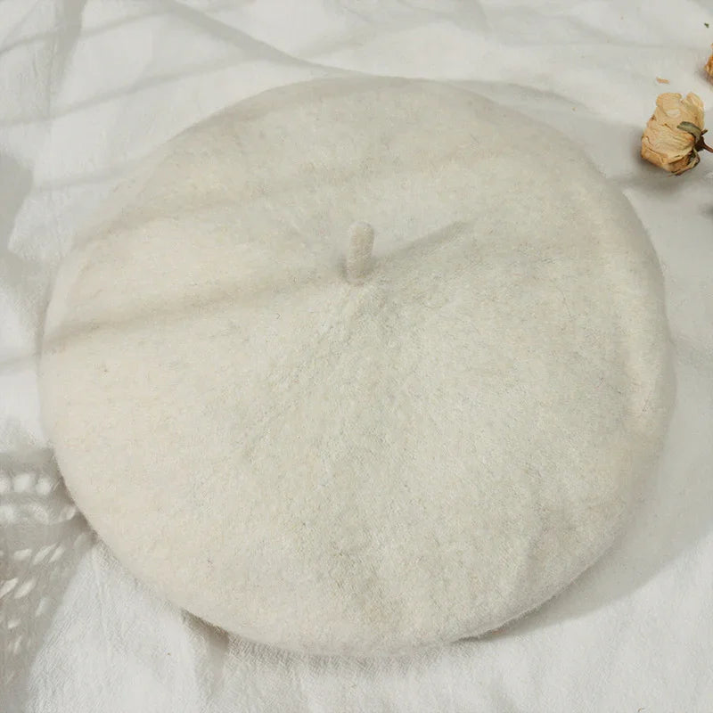 Cream-colored wool beret on white textured fabric with dried flowers nearby