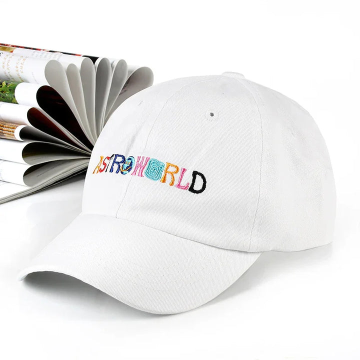 White baseball cap with colorful embroidered ASTROWORLD text on front next to open magazine