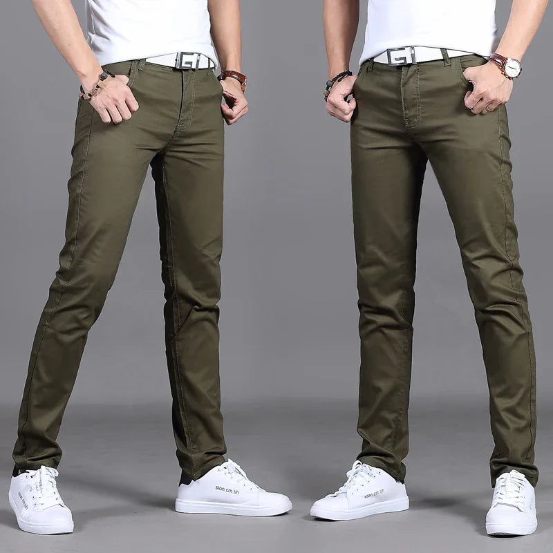 Man wearing slim fit olive green pants with white sneakers and white belt against gray background