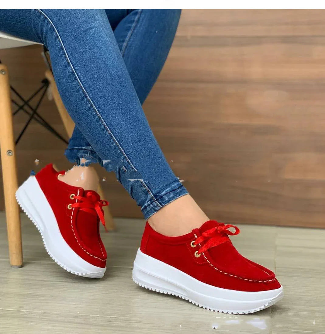 Woman wearing bright red platform sneakers with white soles and blue skinny jeans sitting on wooden chair