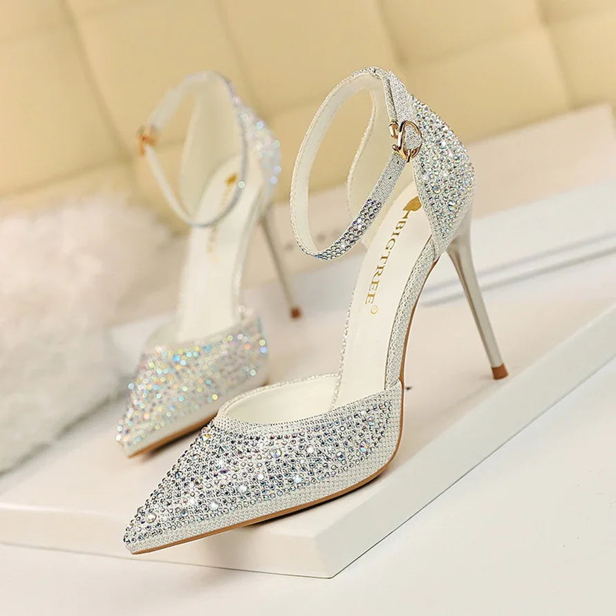 Elegant silver high heel shoes with ankle straps and sparkling rhinestones on a white surface