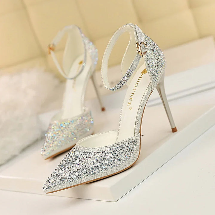 Elegant silver high heel shoes with ankle straps and sparkling rhinestones on a white surface