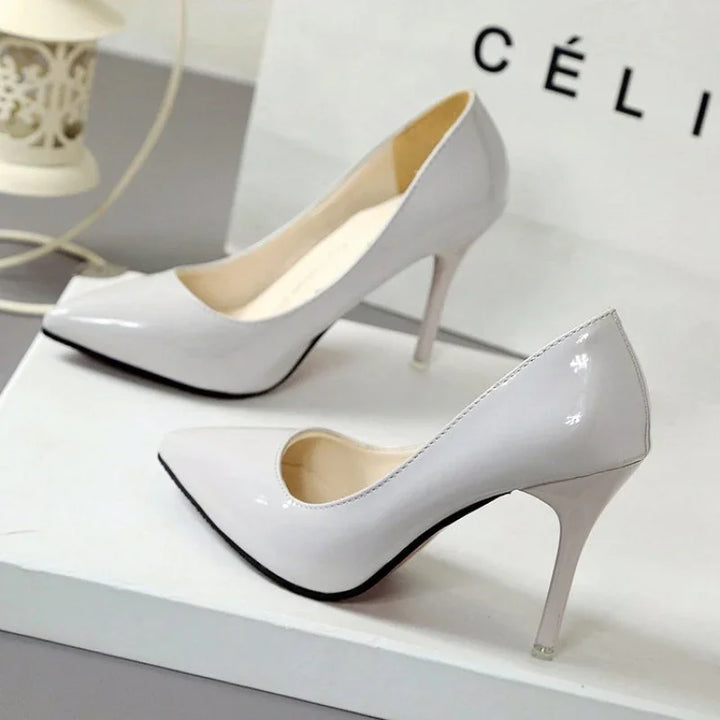 Pair of elegant white patent leather high heels with pointed toes on a white surface
