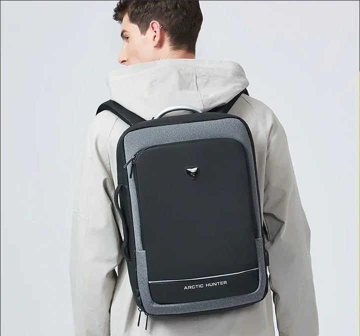 Man wearing gray hooded jacket carrying black and gray Arctic Hunter backpack