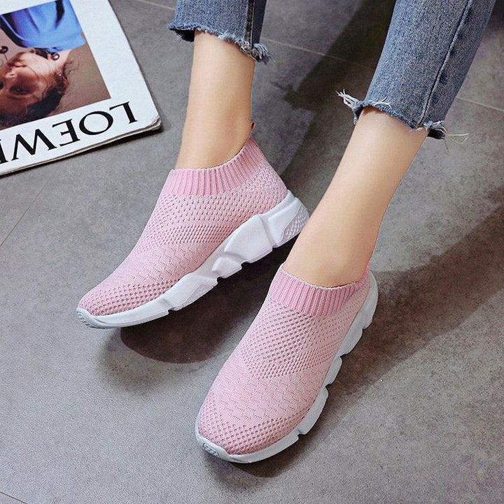 Light pink knitted slip-on sneakers with white soles worn with frayed hem blue jeans on gray floor