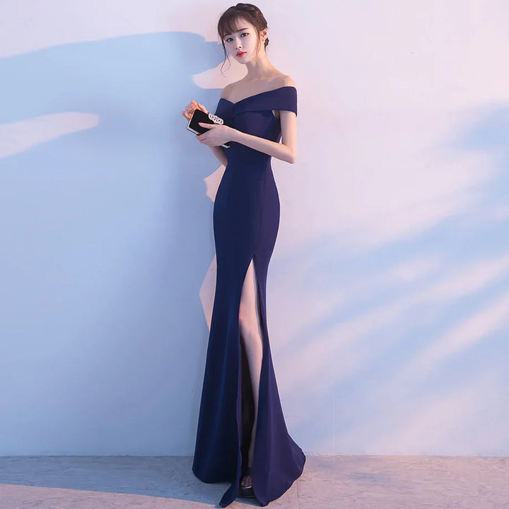 Elegant woman in navy off-shoulder evening gown with thigh-high slit holding black clutch