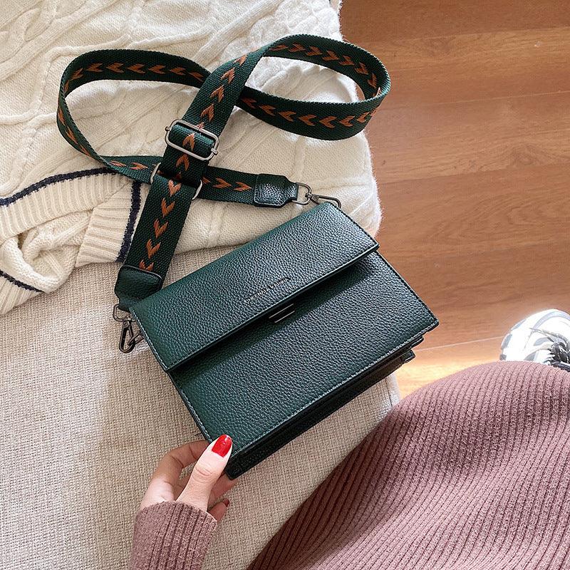 Dark green leather crossbody bag with adjustable patterned strap on cozy knit textiles and wooden floor
