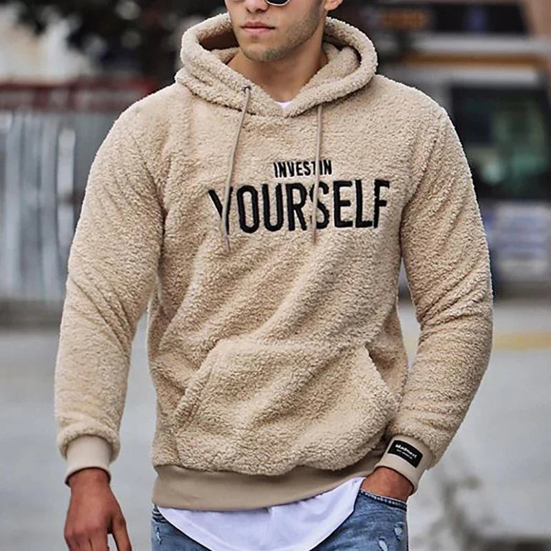 man wearing beige fluffy hoodie with 'Invest in Yourself' text outdoors urban street style