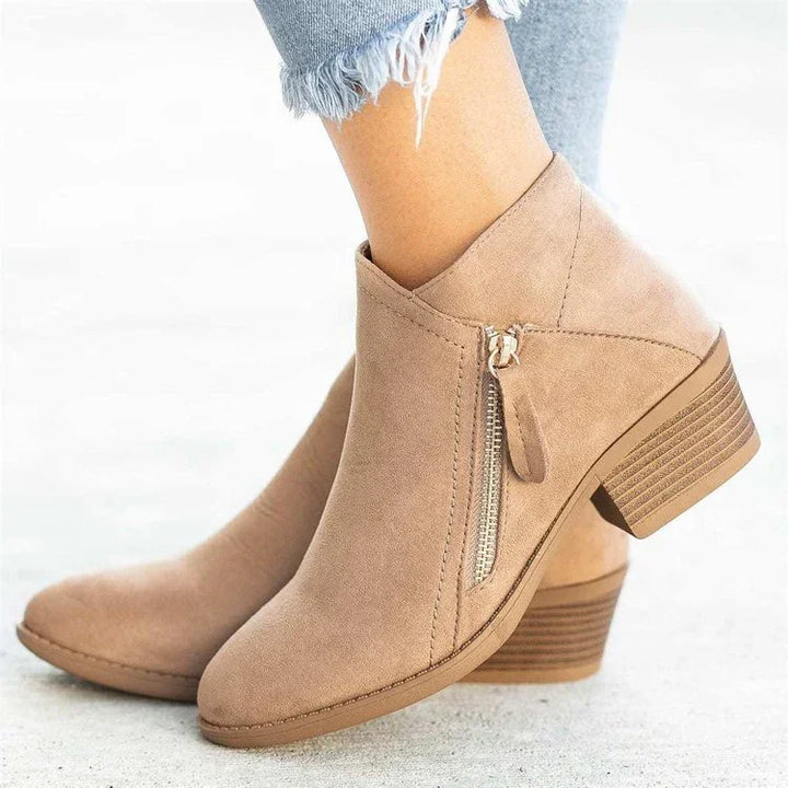 Close-up of beige suede ankle boots with side zipper and block heel worn with frayed hem jeans