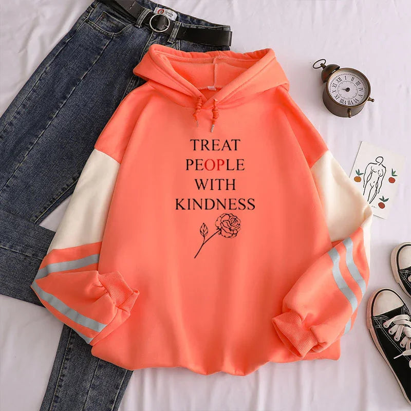 Coral hoodie with white sleeves and reflective stripes, black text 'Treat People With Kindness' and rose graphic, paired with jeans, clock, and sneakers