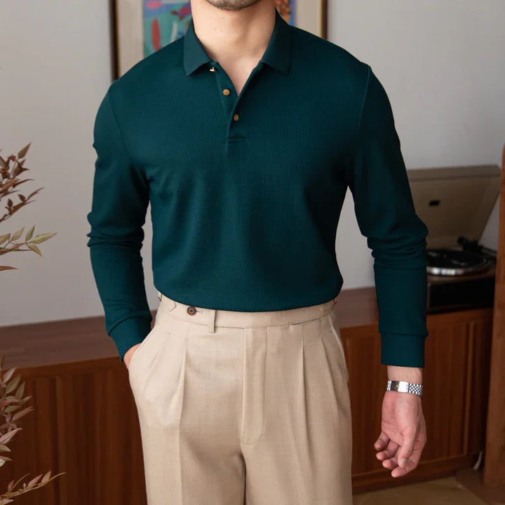 Man wearing dark green long-sleeve polo shirt and beige pleated pants in stylish indoor setting