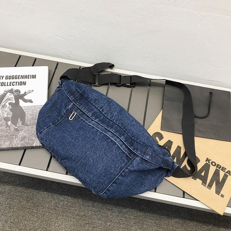 denim blue waist bag with black adjustable strap on gray bench next to magazine and paper bags