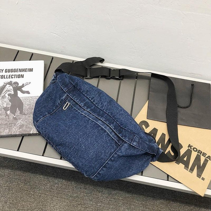 denim blue waist bag with black adjustable strap on gray bench next to magazine and paper bags