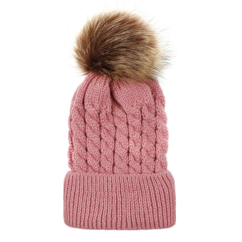 Pink knitted winter beanie hat with cable pattern and brown faux fur pom-pom on white background