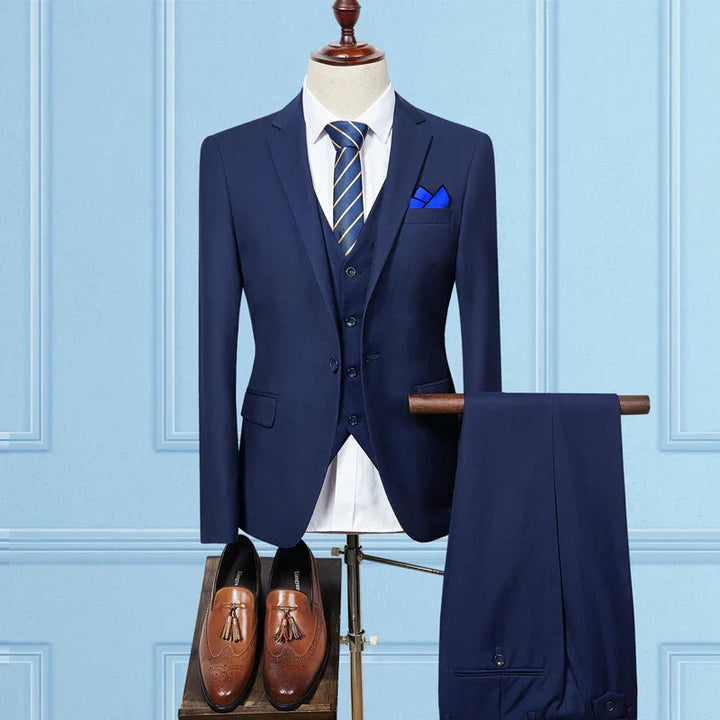 Navy blue men’s three-piece suit with white shirt, striped tie, blue pocket square, and brown tassel loafers