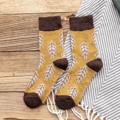 Pair of mustard yellow socks with brown heels, toes, and cuffs, featuring a tree branch pattern on wooden surface with gray striped fabric