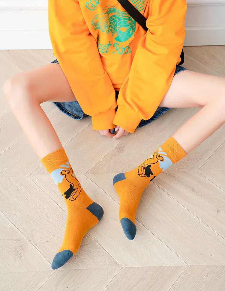 Person wearing bright orange socks with llama design, orange sweatshirt, and denim shorts sitting on light wood floor