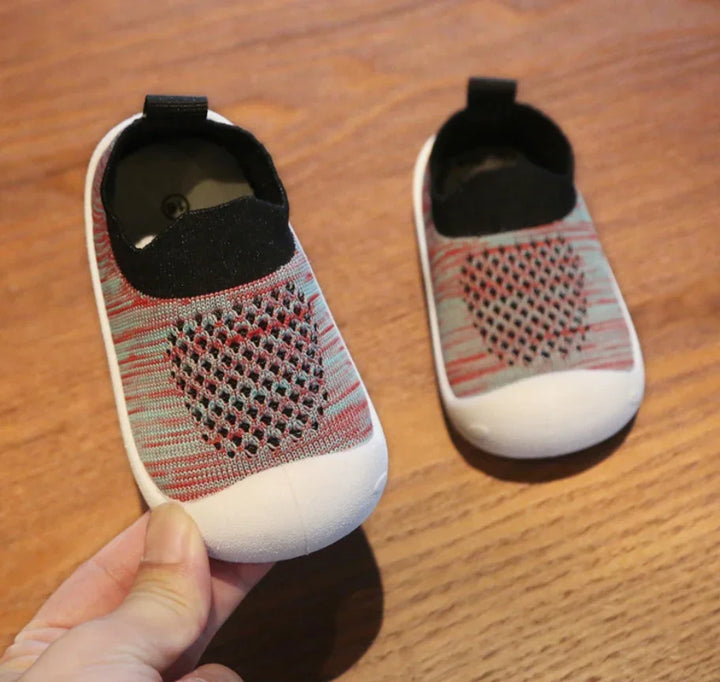 Pair of soft, breathable baby shoes with black and red knit design on wooden floor
