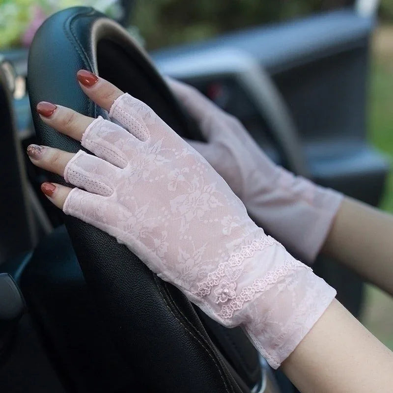 Hands wearing pink floral lace fingerless gloves gripping a black car steering wheel