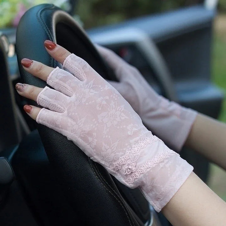 Hands wearing pink floral lace fingerless gloves gripping a black car steering wheel
