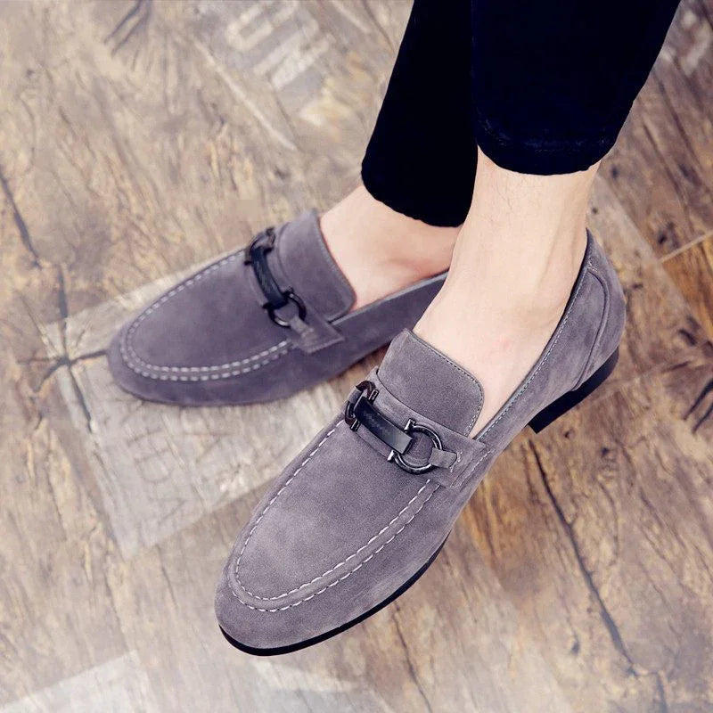Men's grey suede loafers with black metal bit detail worn on wooden floor