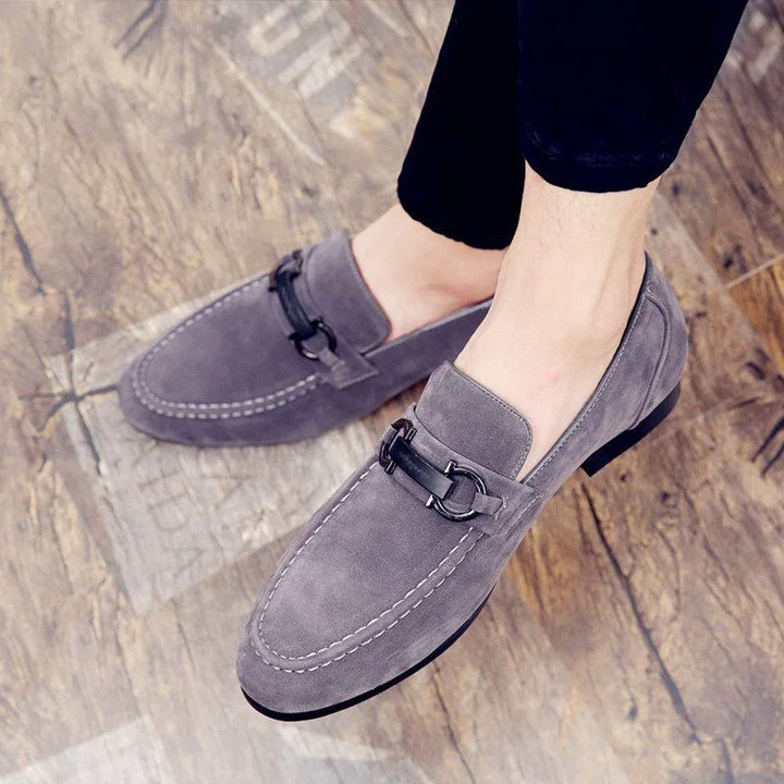 Men's grey suede loafers with black metal bit detail worn on wooden floor