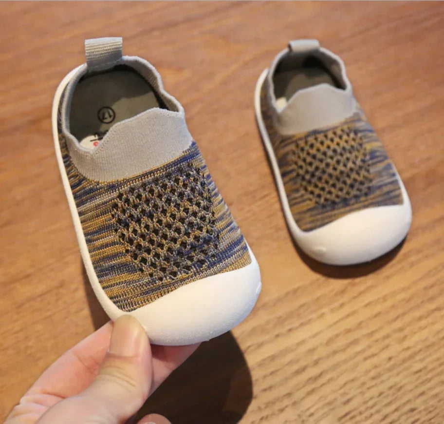 Pair of knitted baby shoes with beige toe caps and textured patterned tops on wooden surface