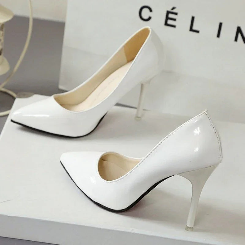 Pair of white patent leather stiletto high heel shoes on a white surface with a CÉLINE logo backdrop