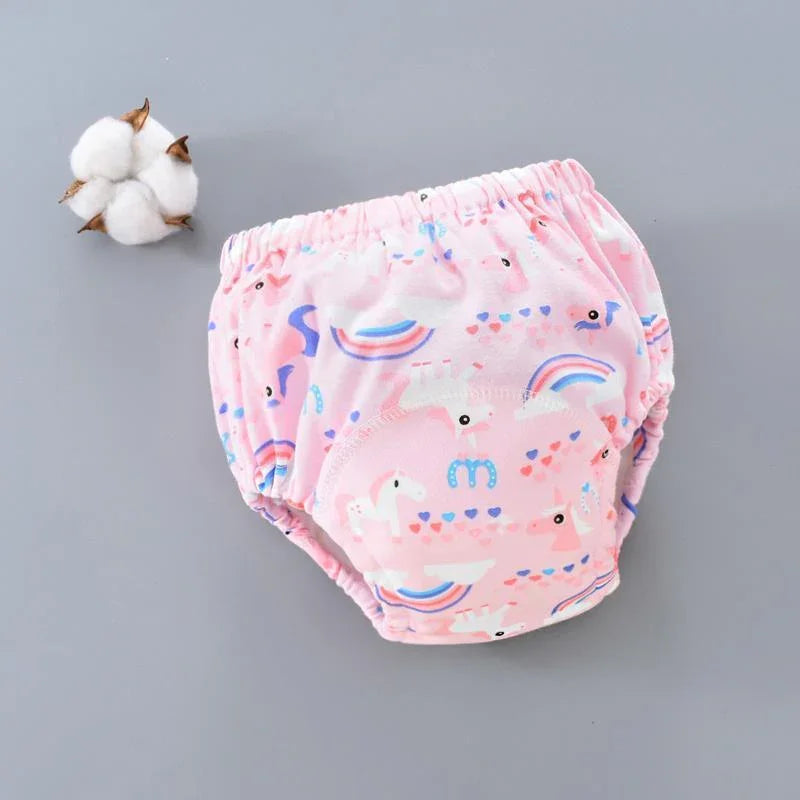 Pink baby training pants with white unicorn, rainbow, and heart patterns on gray background with cotton flower