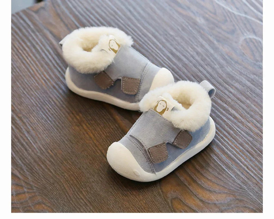 Soft gray baby shoes with white fluffy lining and velcro straps on wooden floor