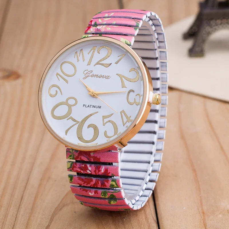 Geneva Platinum wristwatch with large gold numbers and a pink floral stretch band on wooden surface