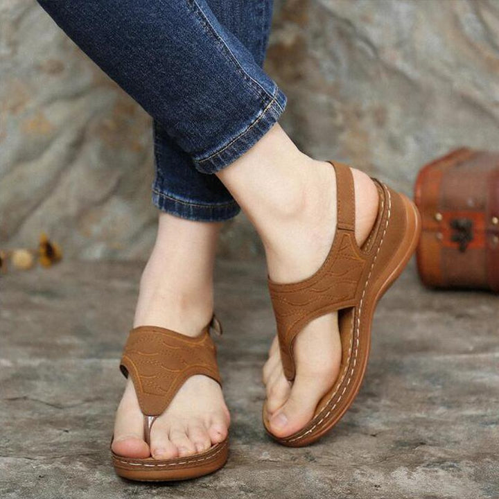Brown leather thong sandals with stitching worn with rolled-up blue jeans on concrete floor