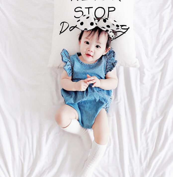 Adorable baby girl in blue romper and polka dot headband lying on white bed with motivational pillow
