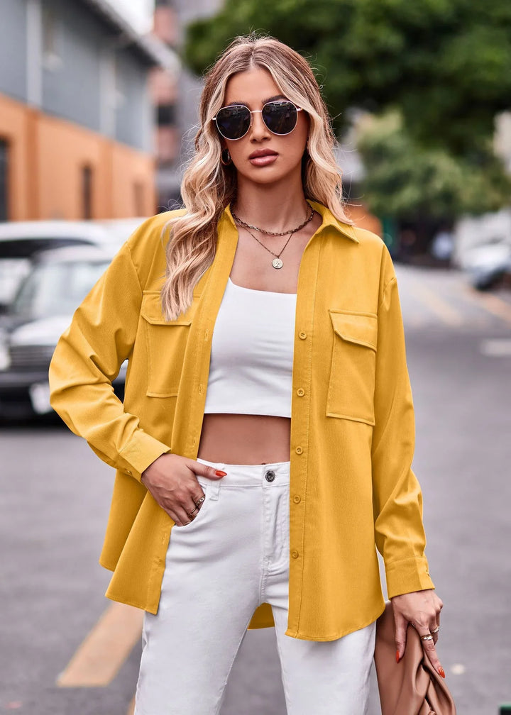Blonde woman wearing yellow button-up shirt, white crop top, and white pants with sunglasses posing on street