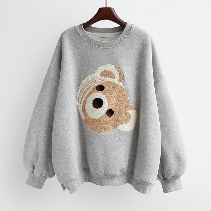Gray sweatshirt with textured teddy bear face graphic on front hanging on wooden hanger